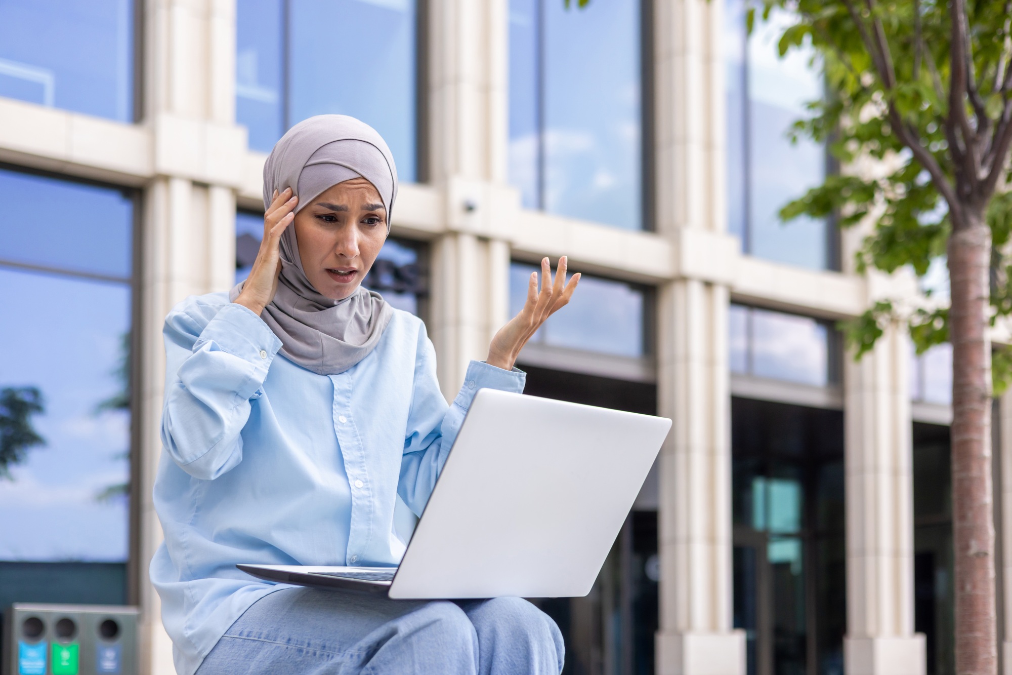 Confused businesswoman in hijab with laptop outdoors